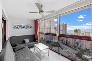 Uma varanda com vista para a paisagem urbana, um sofá cinzento, uma mesa branca e um ventilador de teto.