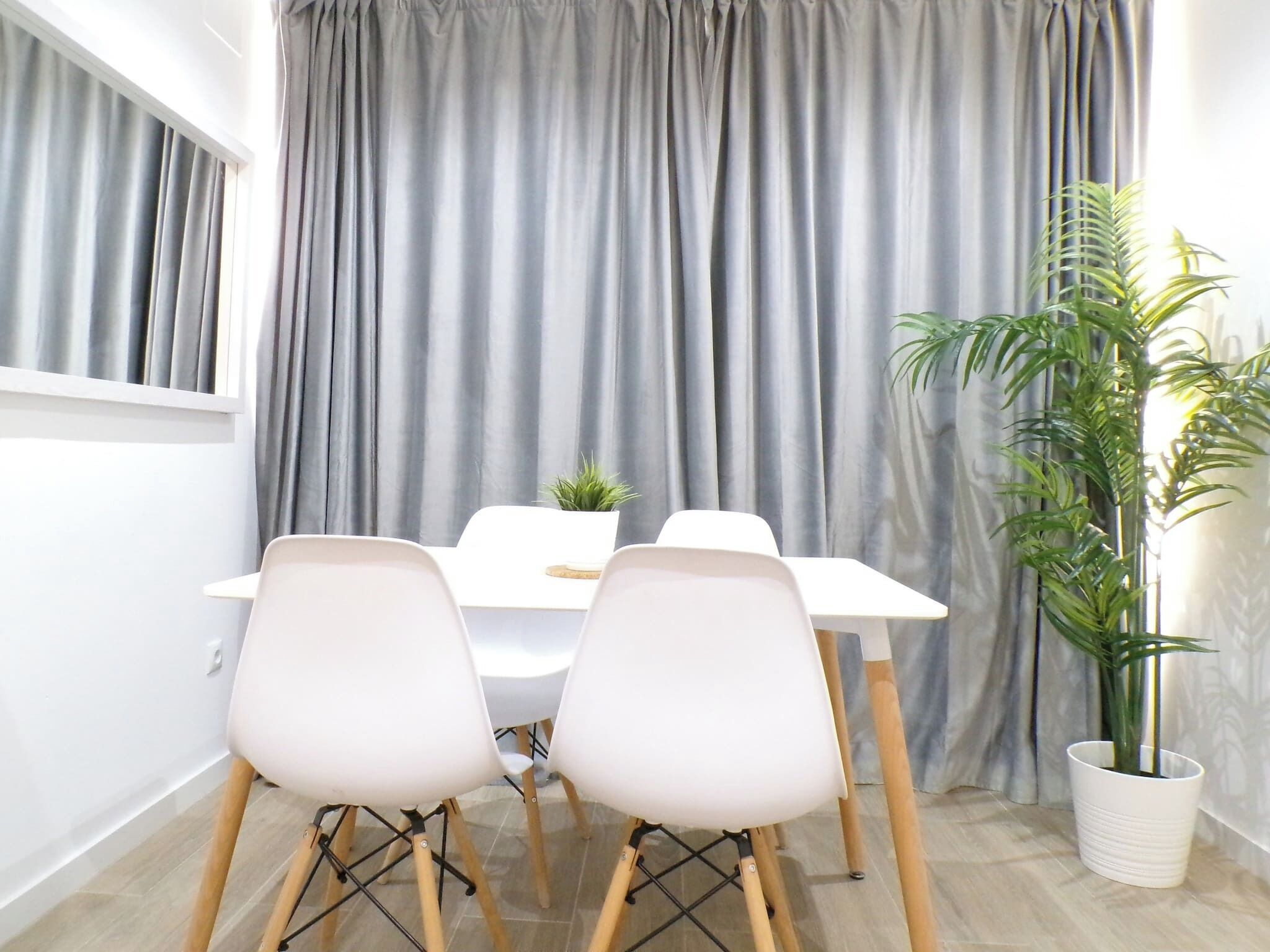 Un comedor con una mesa, cuatro sillas, una planta en maceta y cortinas grises.