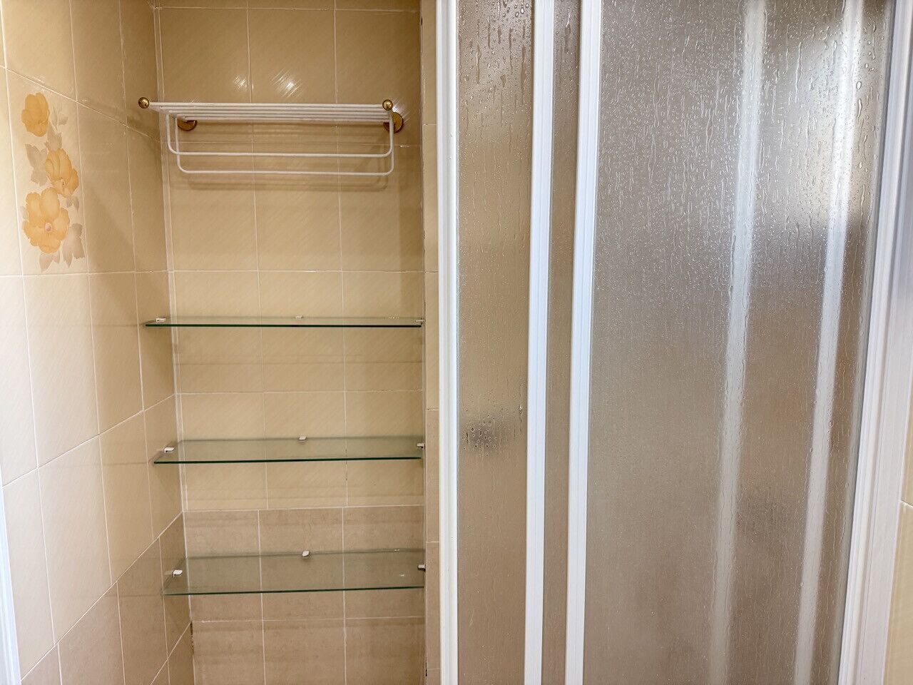 A bathroom with beige tiles, a glass shower enclosure, and a metal towel rack.