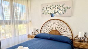Un lit bien fait, avec une literie bleue, une tête de lit en bois, une table de chevet avec une lampe et un tableau de fleurs accroché au mur.
