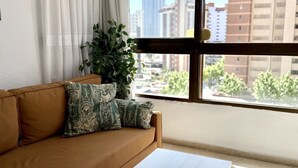 Une pièce avec un canapé, une table, une plante et une fenêtre donnant sur la ville.