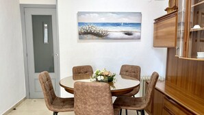 Un coin repas avec une table ronde, quatre chaises, un vase de fleurs et un tableau représentant une scène de plage.