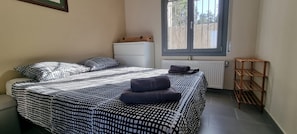 A bedroom with a bed, pillows, a radiator, a window, and a wooden shelf.