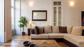 Ein Wohnzimmer mit einem beigefarbenen Ecksofa, einem Holztisch, einem Blumentopf und einem Spiegel an der Wand.