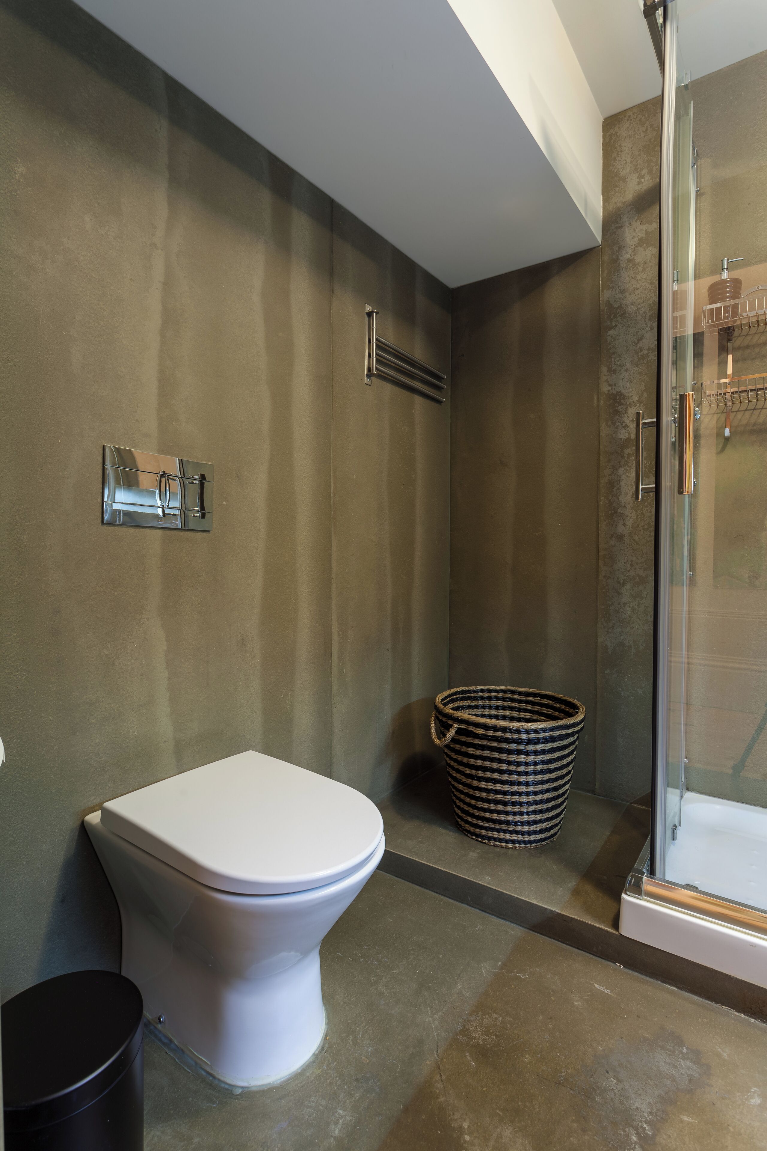 Une salle de bain avec des toilettes blanches, une douche en verre et un panier en osier posé sur le sol.