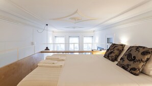 Ein Hotelzimmer mit einem großen Bett, einem Holzkopfende und Blick auf die Stadt durch große Fenster.
