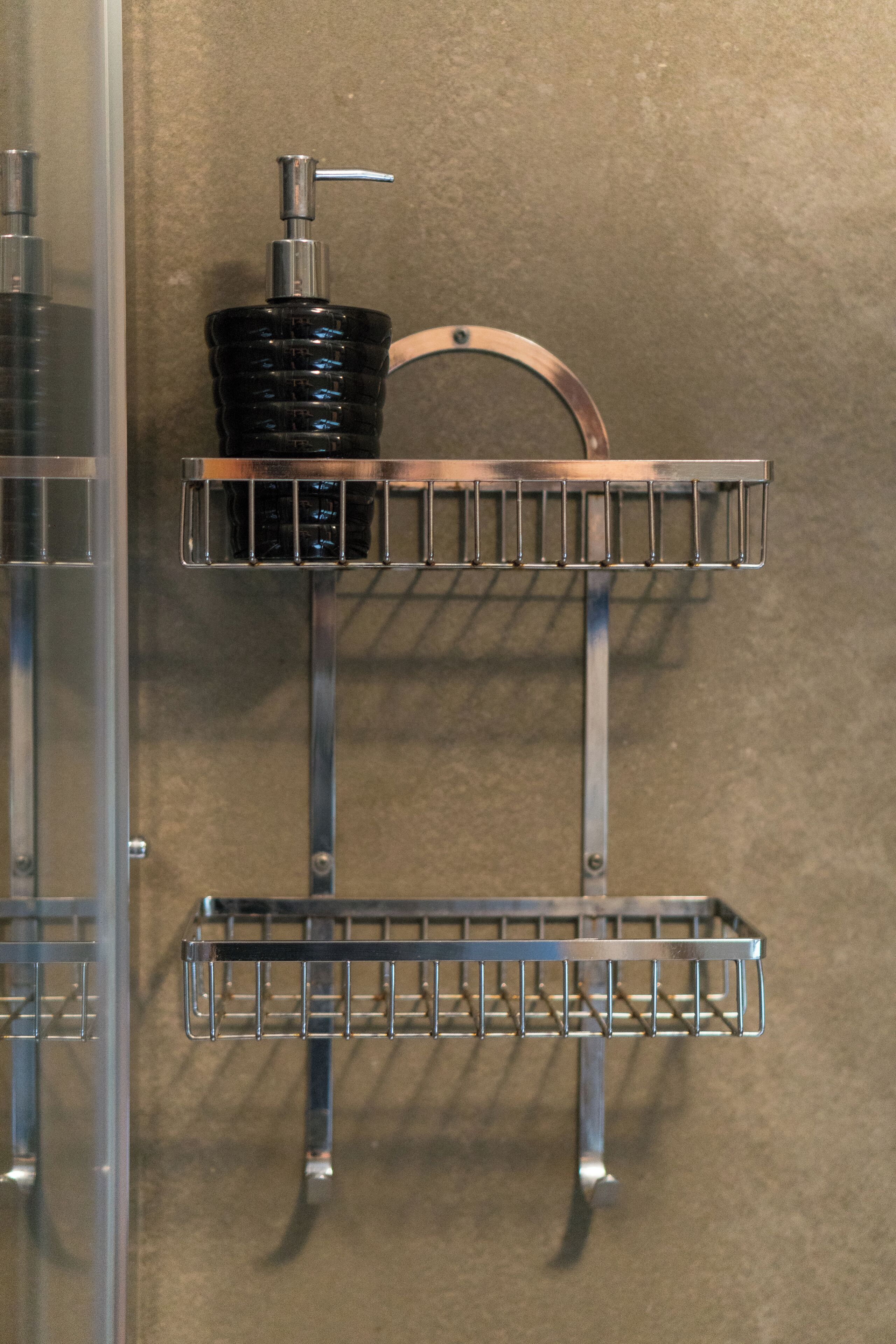 A bathroom with a metal shelf holding a black bottle and a metal rack.