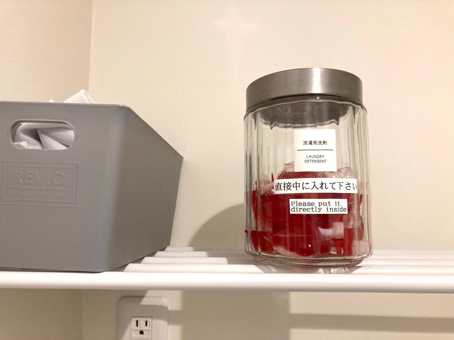 A bathroom with a tissue box and a glass container of laundry detergent on a shelf.