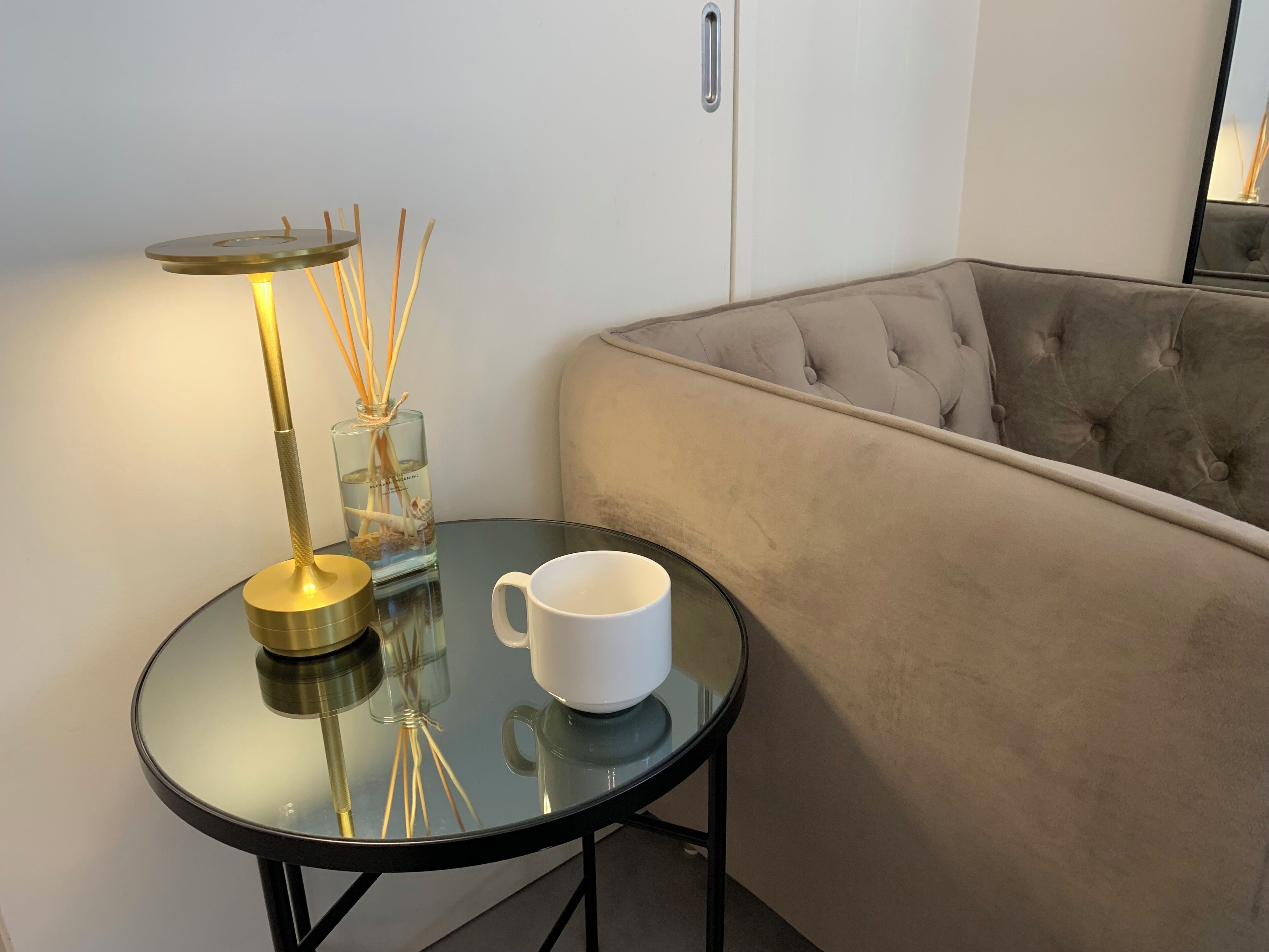 A round glass table with a white mug and a lamp with a glass base.