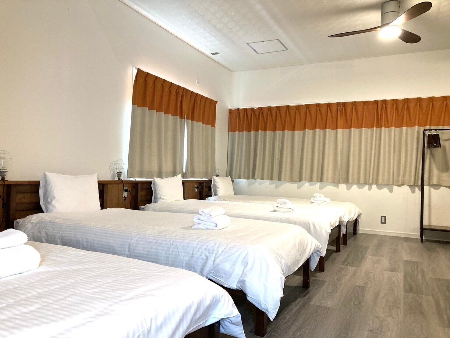 A hotel room with three beds, a ceiling fan, and a window with curtains.