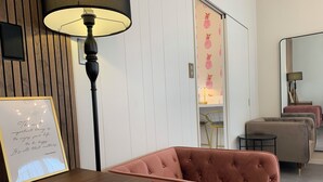 Una habitació amb un escriptori de fusta, una cita inspiradora emmarcada, una cadira amb tapisseria rosa, una làmpada i un mirall.