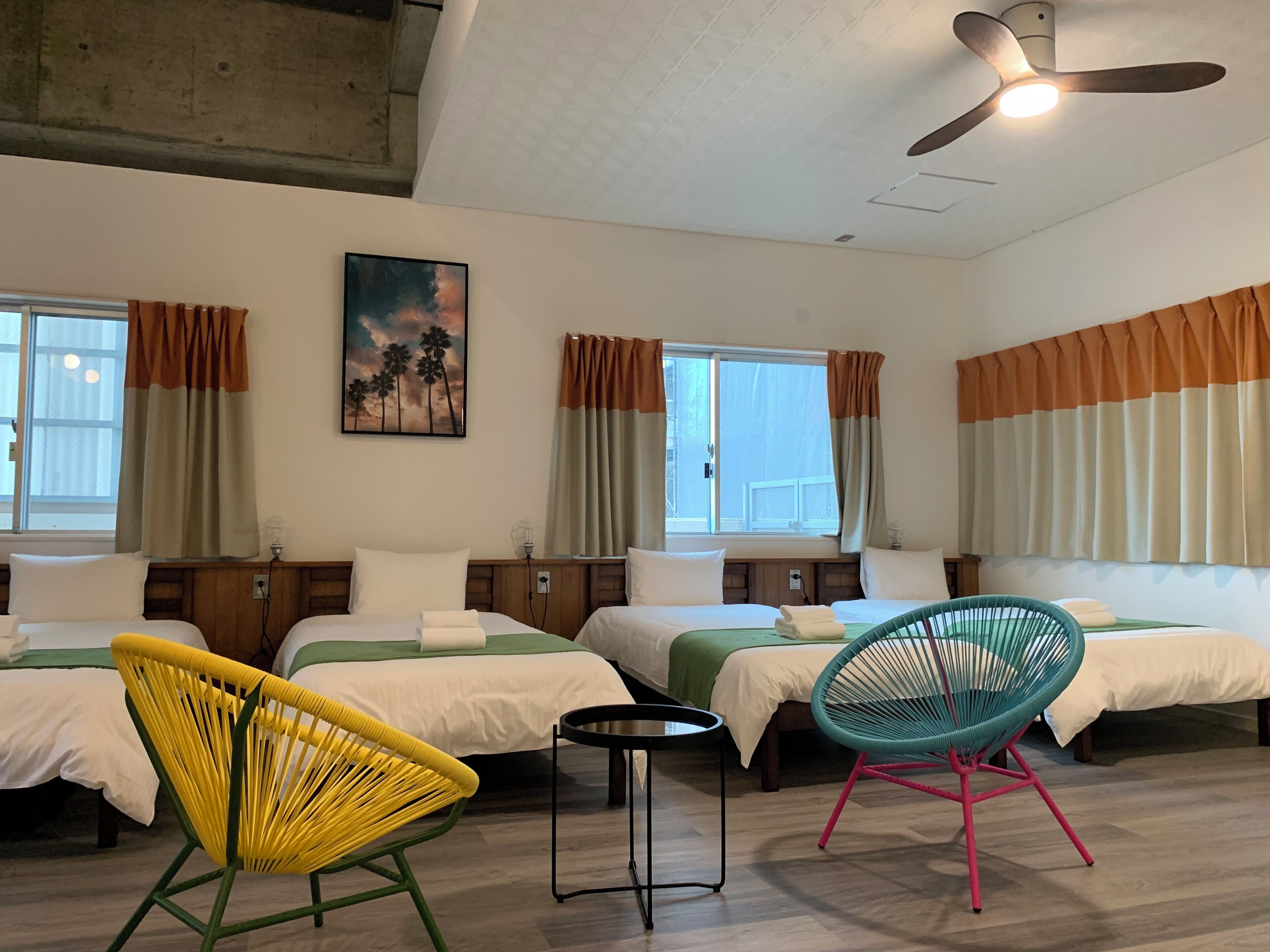 A hotel room with two beds, a ceiling fan, and a painting of palm trees.