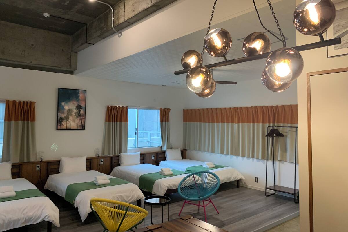 Habitació d'hotel amb quatre llits, ventilador de sostre i una finestra gran amb cortines.