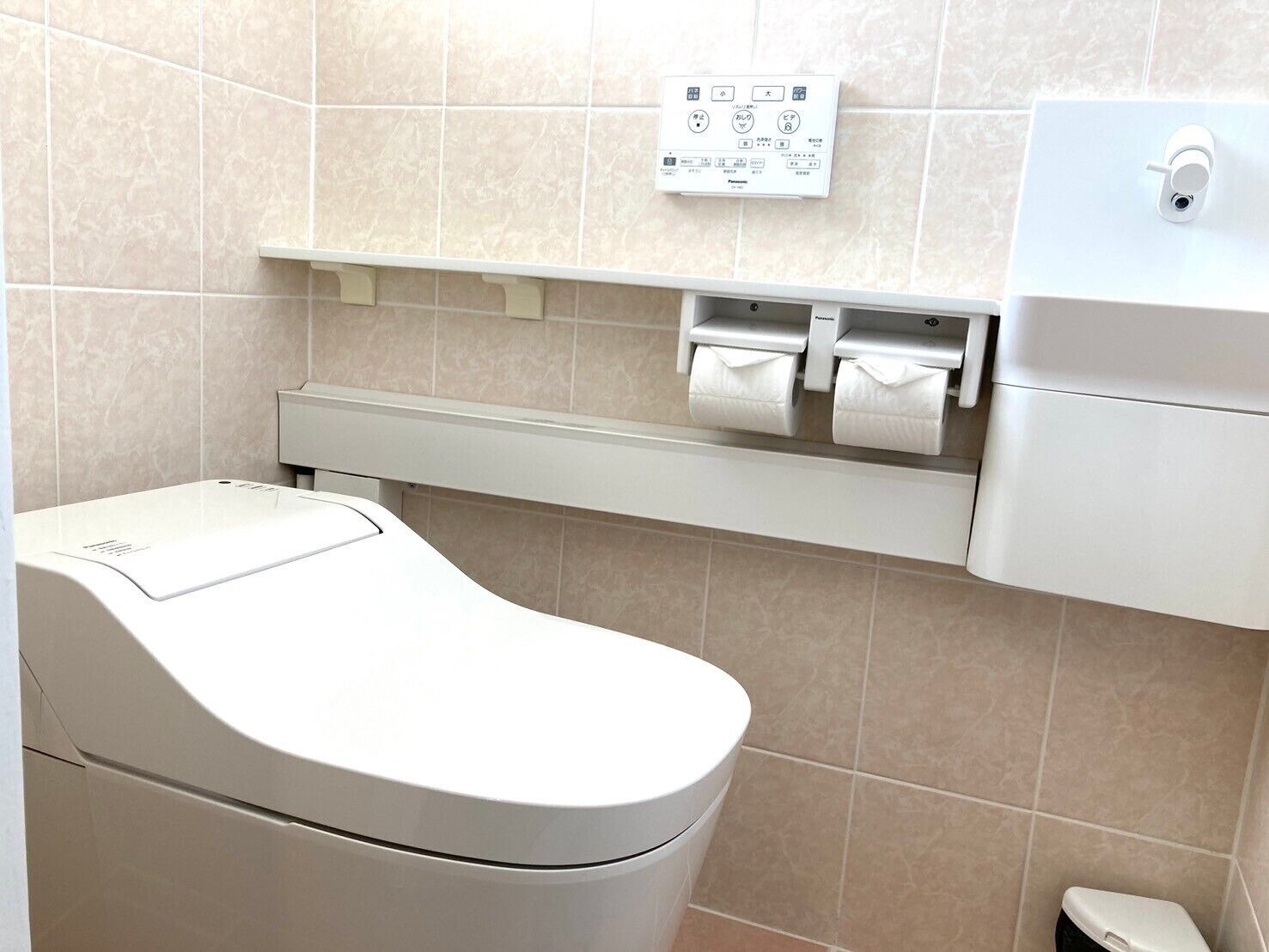 A modern bathroom with a toilet, a paper towel dispenser, and a soap dispenser on a wall.