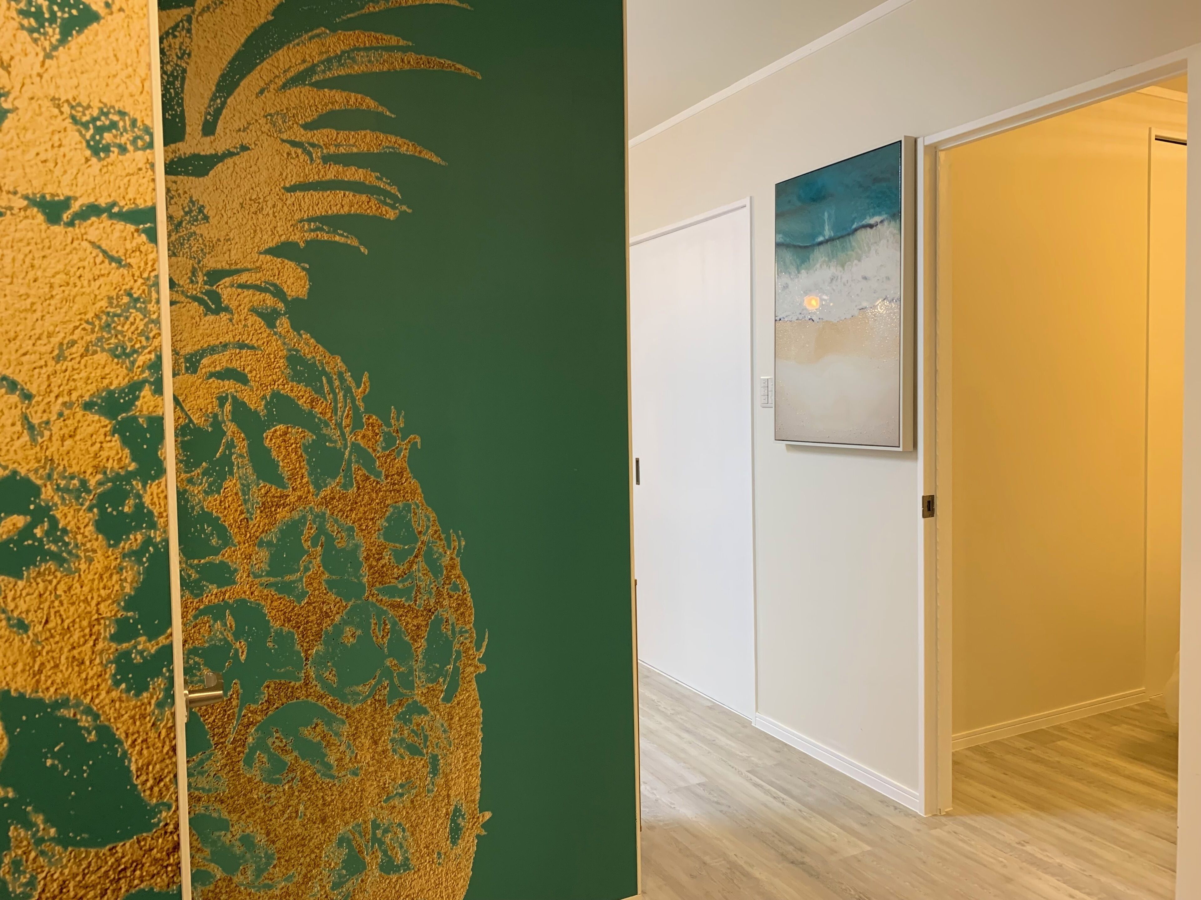 Un couloir avec un mur vert à texture, un plancher en bois et une porte ornée d’un tableau.