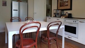 Cocina compacta con armarios blancos, estufa y cafetera. Cuenta con una mesa de comedor y cuatro sillas.