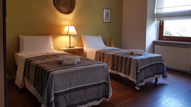Habitación de hotel con dos camas, una lámpara, un cuadro en la pared y una ventana con persianas.