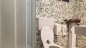 Een badkamer met toilet, bidet, douchecabine van glas en een betegelde wand.