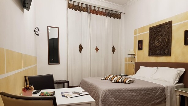 Een hotelkamer met een bed, een bureau, een stoel, een spiegel, een raam met gordijnen en een wand met decoratief paneel.