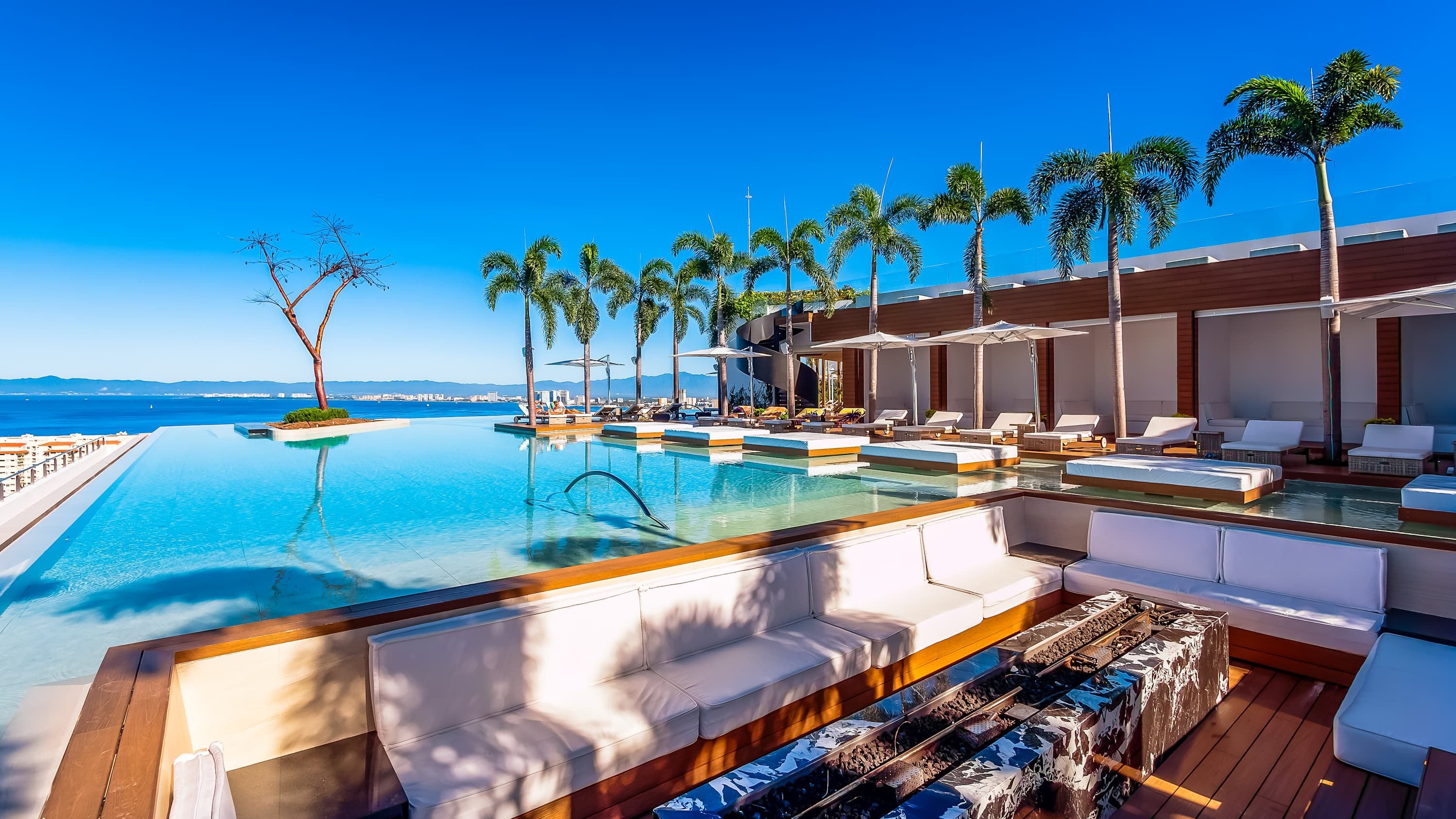 A poolside area with lounge chairs, a wooden deck, and palm trees.