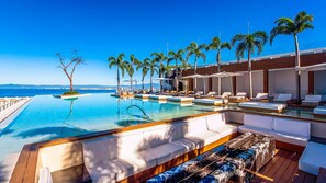 A poolside area with lounge chairs, a wooden deck, and palm trees.