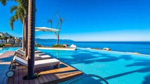 A clear blue sky, a swimming pool with lounge chairs, and a view of the sea.