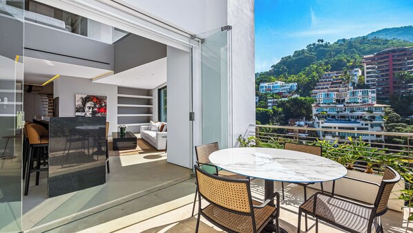 A modern balcony with a glass door leading to a living area, a round table, and wicker chairs.