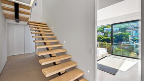 A modern staircase with wooden steps and a glass door leading to a balcony with a city view.