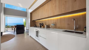 A modern kitchen with white cabinetry, a stainless steel sink, and a view of the ocean.