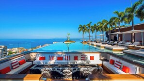 A poolside area with lounge chairs, a hot tub, and a view of the ocean.