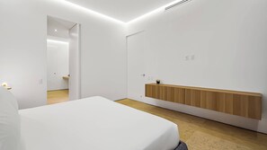 A modern bedroom with a large bed, a wooden bedside unit, and a minimalist design.