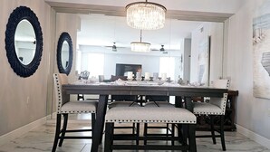 Un coin repas comprenant une grande table, quatre chaises rembourrées, un lustre et un tableau accroché au mur.