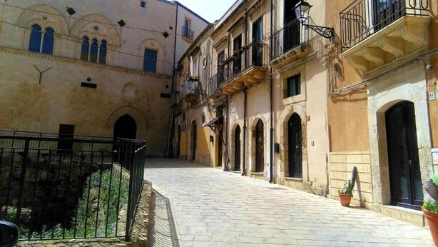 A narrow cobblestone street flanked by historic buildings with arched doorways and balconies.