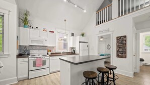 A spacious kitchen with white cabinetry, a central island with stools, and a view of the upper floor.