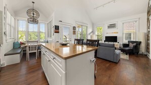 Una cocina amplia con una isla grande, armarios blancos y una zona de comedor con un banco y sillas.
