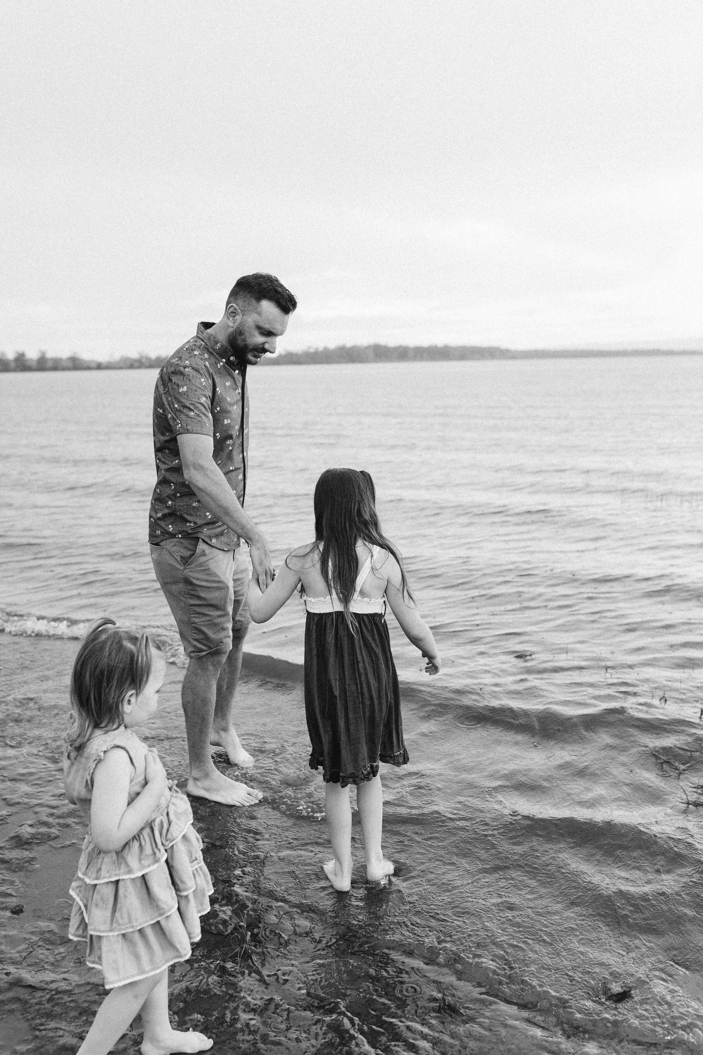 Una familia de tres en una playa con mar tranquilo y cielo nublado.