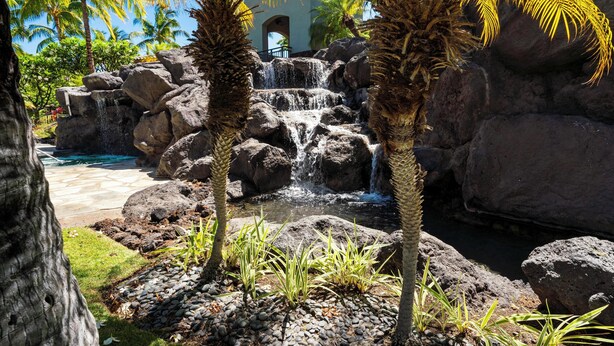 A tropical garden with a waterfall, palm trees, and a pool. - Mauna Lani Beach Club Pass included!  701 Fairways at Mauna Lani (Mauna Lani Resort)