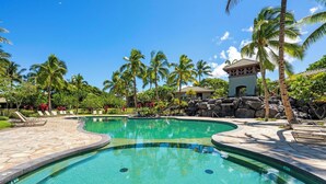 A swimming pool with a curved design, surrounded by palm trees and a small building with a tiled roof. - Mauna Lani Beach Club Pass included!  701 Fairways at Mauna Lani (Mauna Lani Resort)