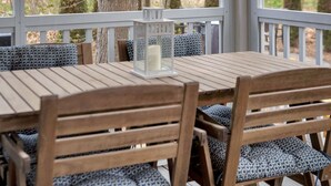 A wooden deck with a table and chairs, overlooking a forest.