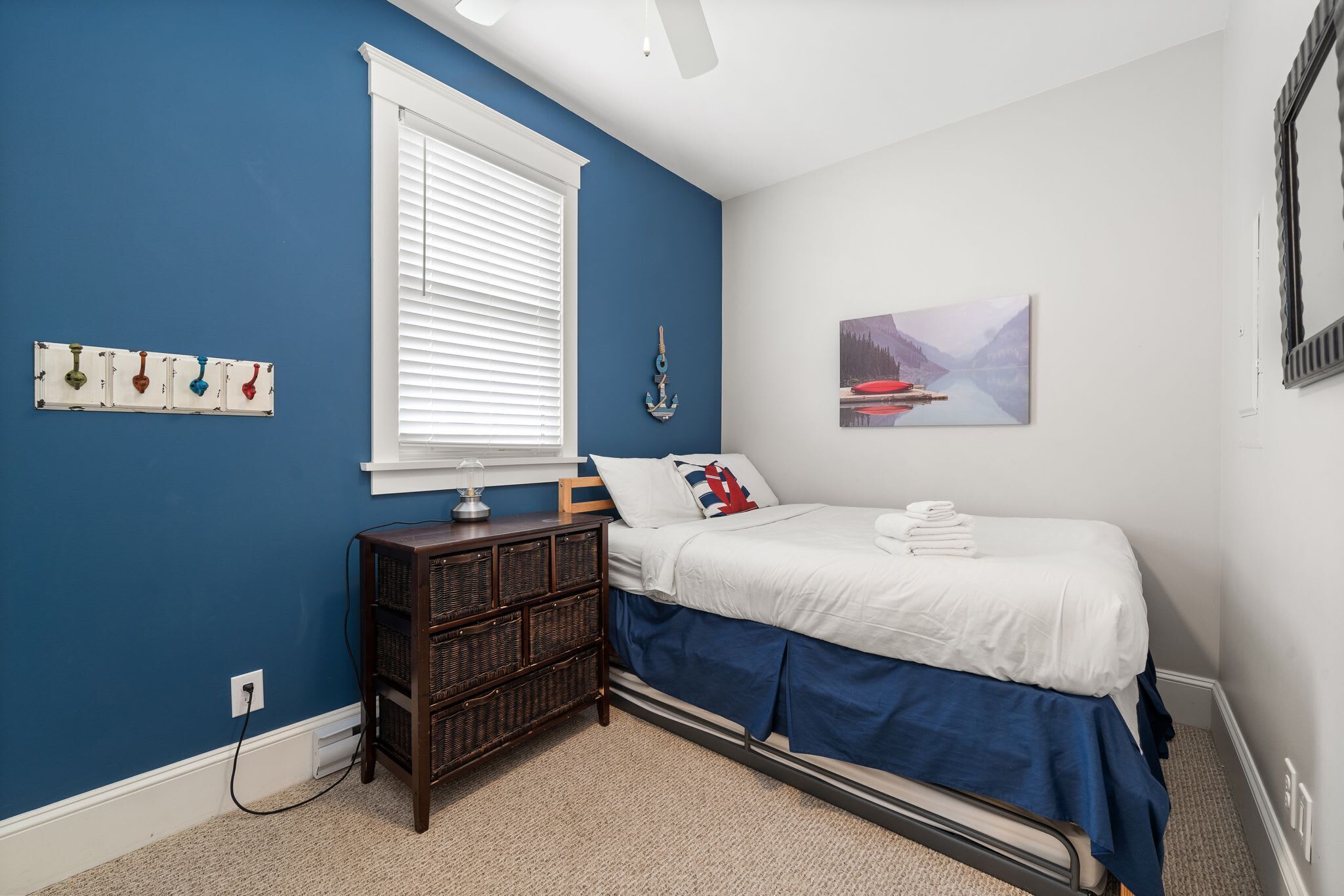 A bedroom with a single bed, a nightstand, a dresser, a window with blinds, and a wall-mounted picture.