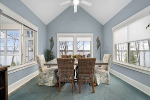 A dining room with a high ceiling, large windows, and a view of the outdoors.