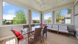 A covered patio with a glass-top table, wicker chairs, a sofa, and a ceiling fan.