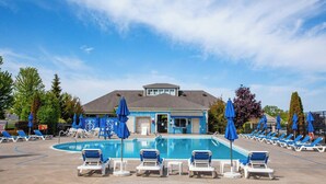 A swimming pool with lounge chairs and umbrellas, a building with a blue facade, and trees in the background. - The Rushes - 47 Butternut (Prince Edward)