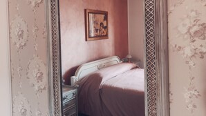 Een slaapkamer met een grote, versierde spiegel, bloemenbehang, een bed met hoofdeinde en een nachtkastje.