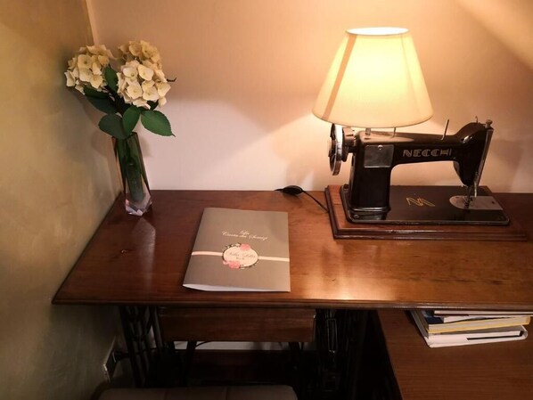 Une table en bois avec une machine à coudre, une lampe, un vase de fleurs et un classeur.