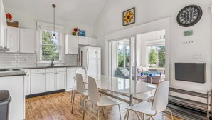 Une cuisine moderne avec des meubles blancs, un réfrigérateur en acier inoxydable, une table à manger avec des chaises et une grande fenêtre.