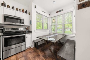 A kitchen with white cabinets, stainless steel appliances, a wooden dining table, and a bench.