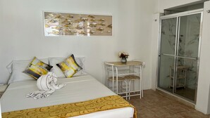 Ein Hotelzimmer mit einem Bett, einem kleinen Tisch mit Blumenvase, einer Glasdusche und einem Wandbild.