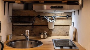A compact kitchen with wooden cabinets, a stainless steel sink, a built-in stove, and a hanging utensil rack. - Renovated Provencal studio, in the heart of the village of Eyragues, beautiful flower-filled courtyard (Eyragues)