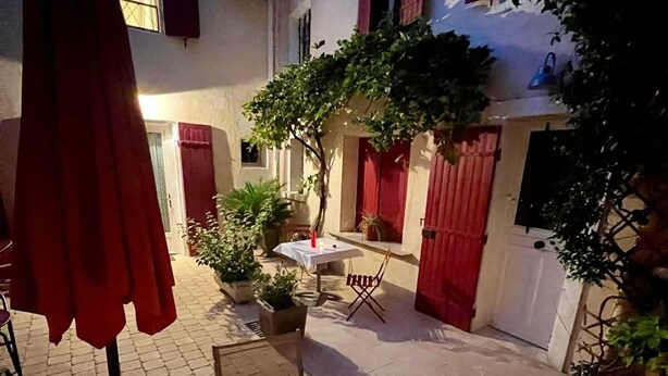 An outdoor patio area with a round table, chairs, and a red umbrella. - Renovated Provencal studio, in the heart of the village of Eyragues, beautiful flower-filled courtyard (Eyragues)